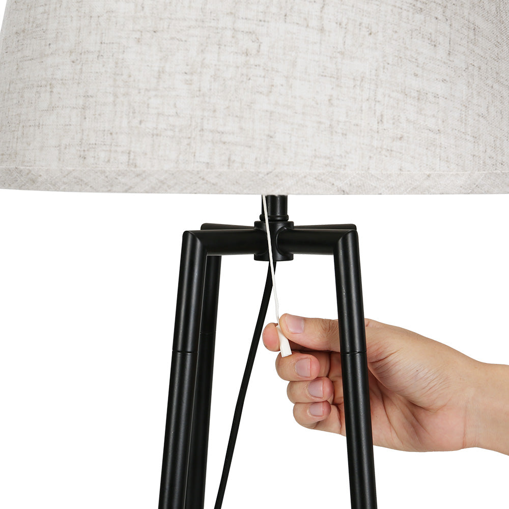 Hand adjusting black metal frame switch beneath beige linen lampshade, showcasing retro vintage style and quality home decor .