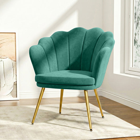 Green velvet vintage armchair with scalloped shell back and brass tapered legs in bright sunlit corner, retro home decor.