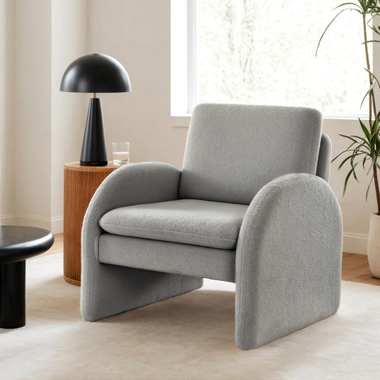 Grey boucle vintage armchair with curved arms and retro velvet texture in bright modern living room setting with wooden side .