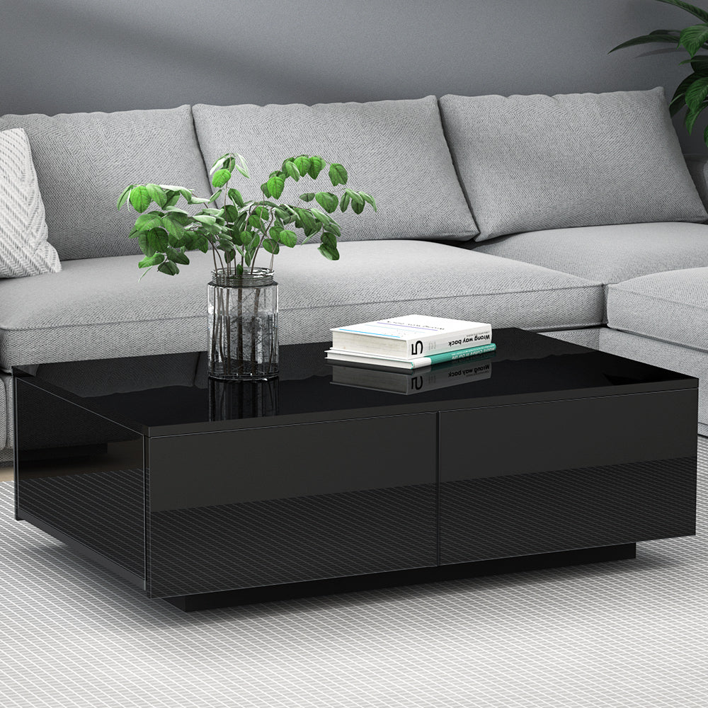 Black glossy coffee table with four drawers in a modern living room, paired with a light gray velvet vintage-style sofa,.