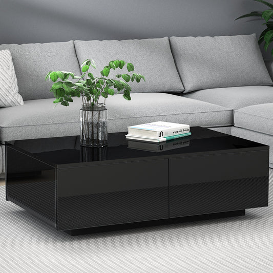 Black glossy coffee table with four drawers in a modern living room, paired with a light gray velvet vintage-style sofa,.