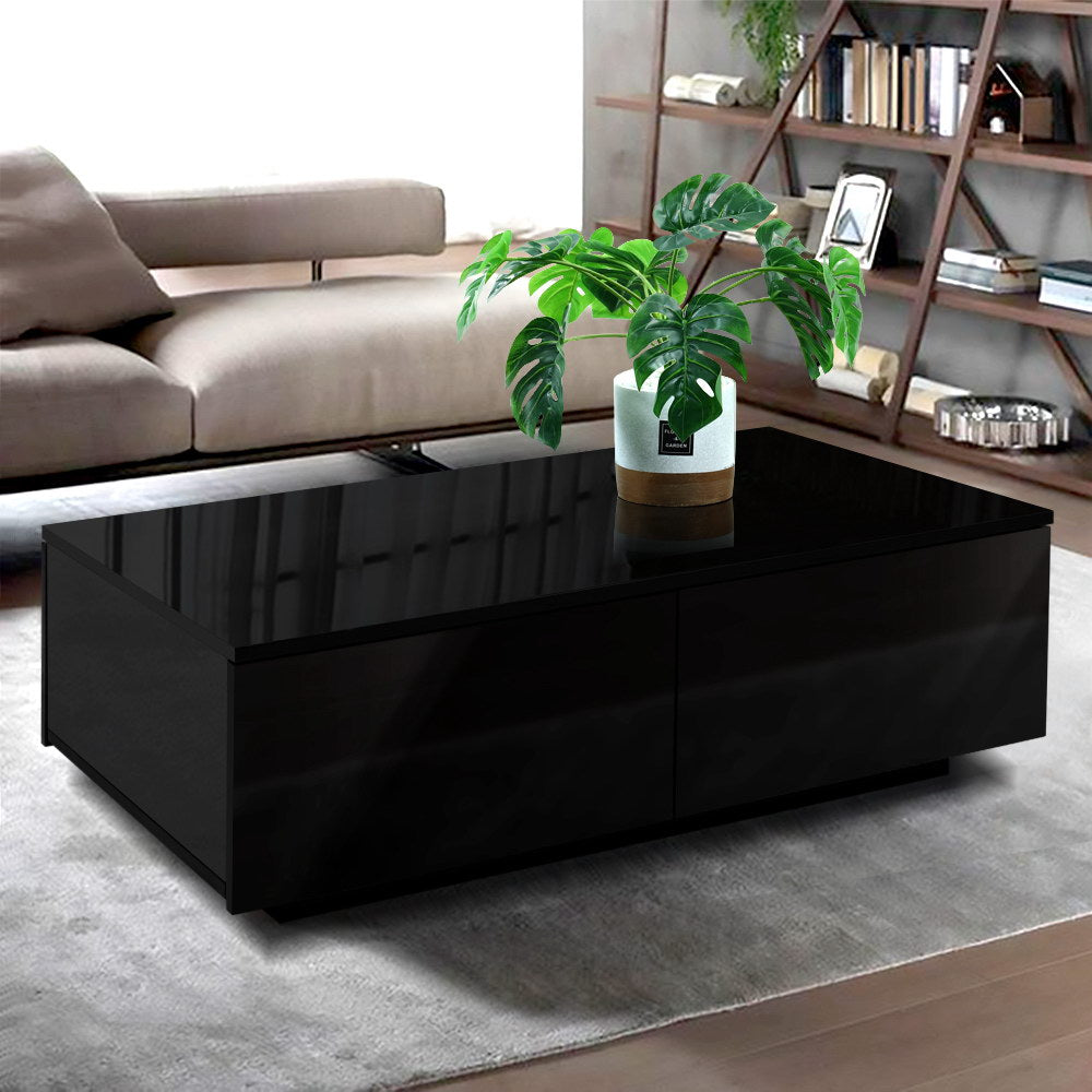 Black glossy Artiss Coffee Table with four drawers, sleek retro design in a modern living room with beige sofa, wooden.