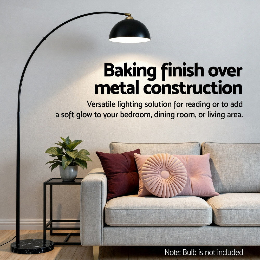 Black arched floor lamp with baking finish metal, heavy marble base beside gray sofa with retro velvet cushions in stylish.