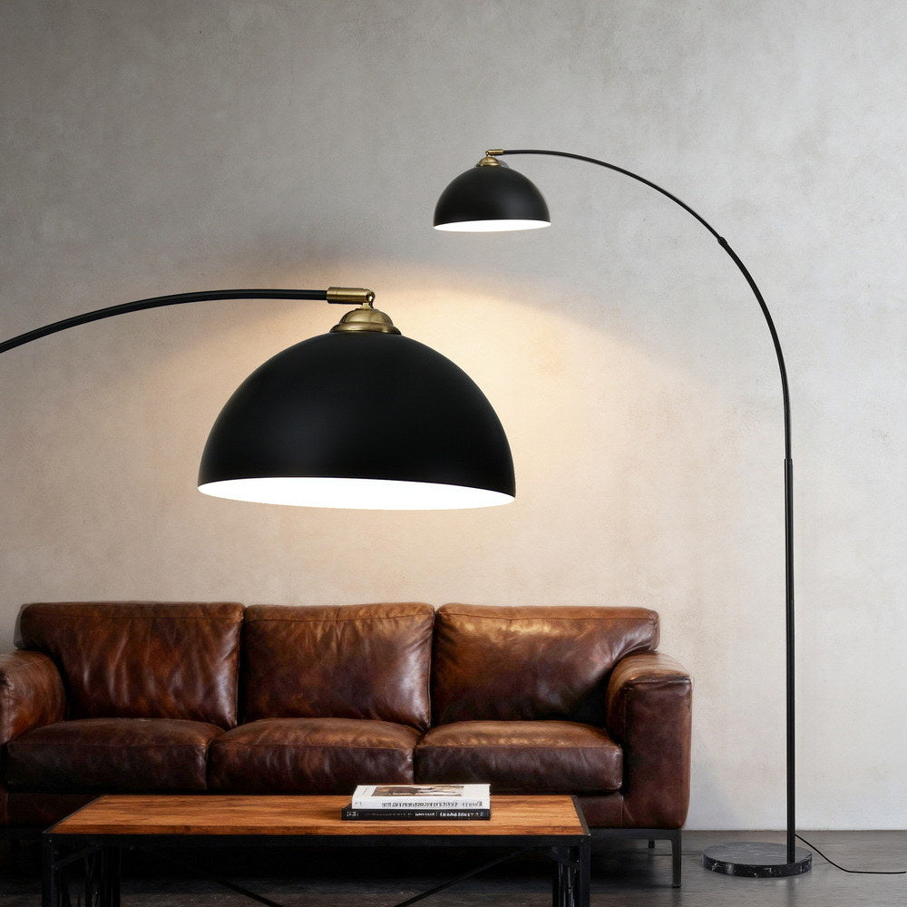 Black modern arched floor lamp with heavy-duty marble base illuminating vintage brown leather sofa in stylish living room.