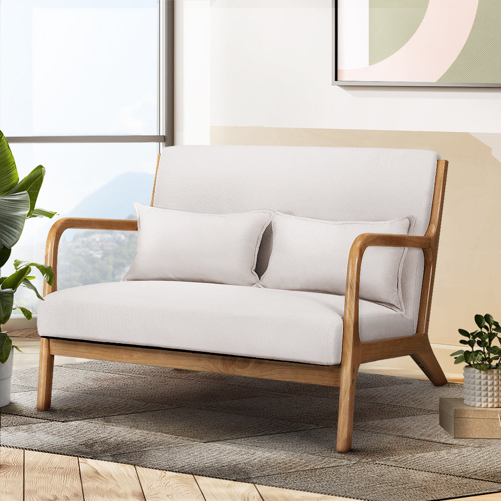 Beige velvet retro loveseat with wooden frame and curved armrests in bright living room featuring houseplants and modern.