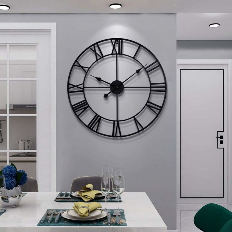 Large black wall clock on a gray wall above a dining table with glasses and plates.