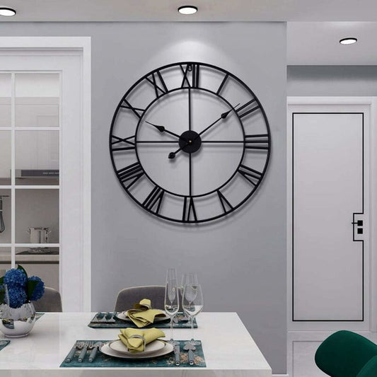 Large black wall clock on a gray wall above a dining table with glasses and plates.