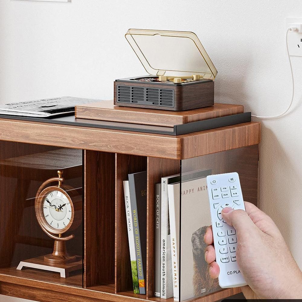 Wooden shelf with a record player, books, and a clock, with a hand holding a remote control.