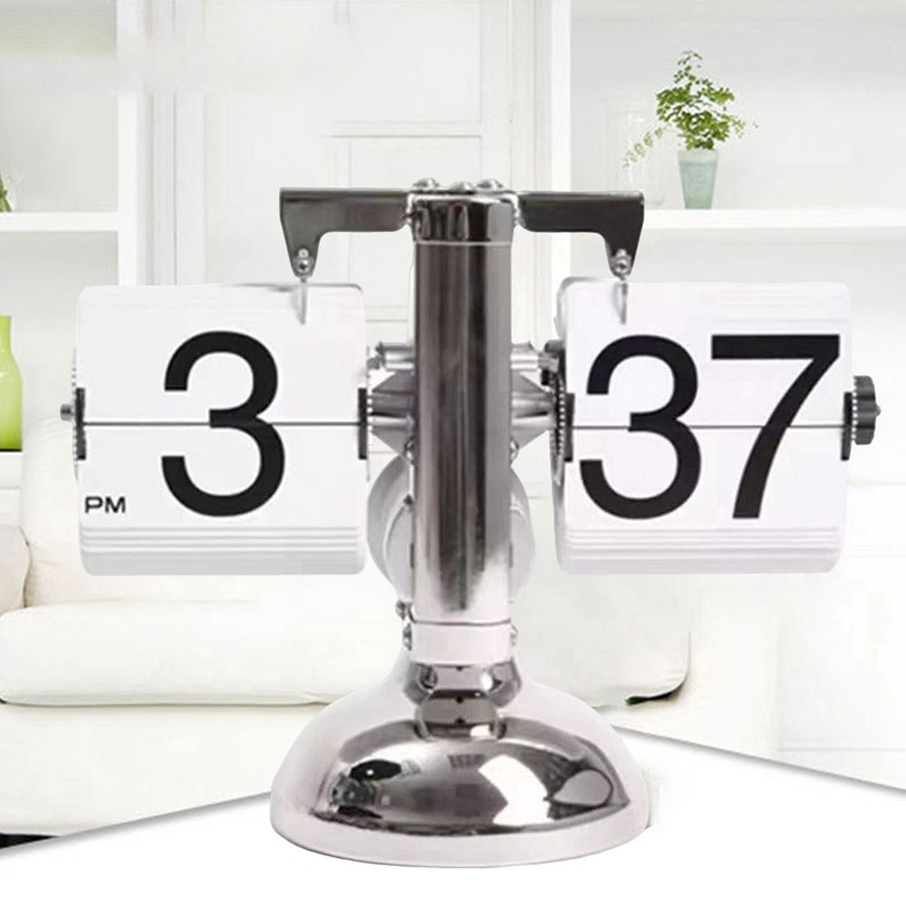 A modern chrome flip clock showing 3:37 PM, set against a bright, modern living room background with a white sofa and shelving.