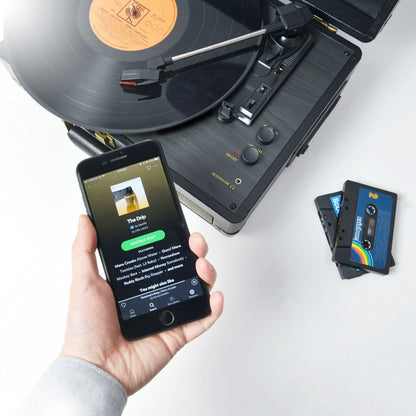 Black retro velvet mbeat Uptown Retro Turntable with Bluetooth and cassette player on white surface, hand holding smartphone .