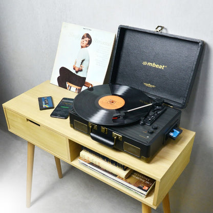 Retro mbeat Uptown vinyl turntable and cassette player in a black velvet suitcase style on a mid-century wood side table.