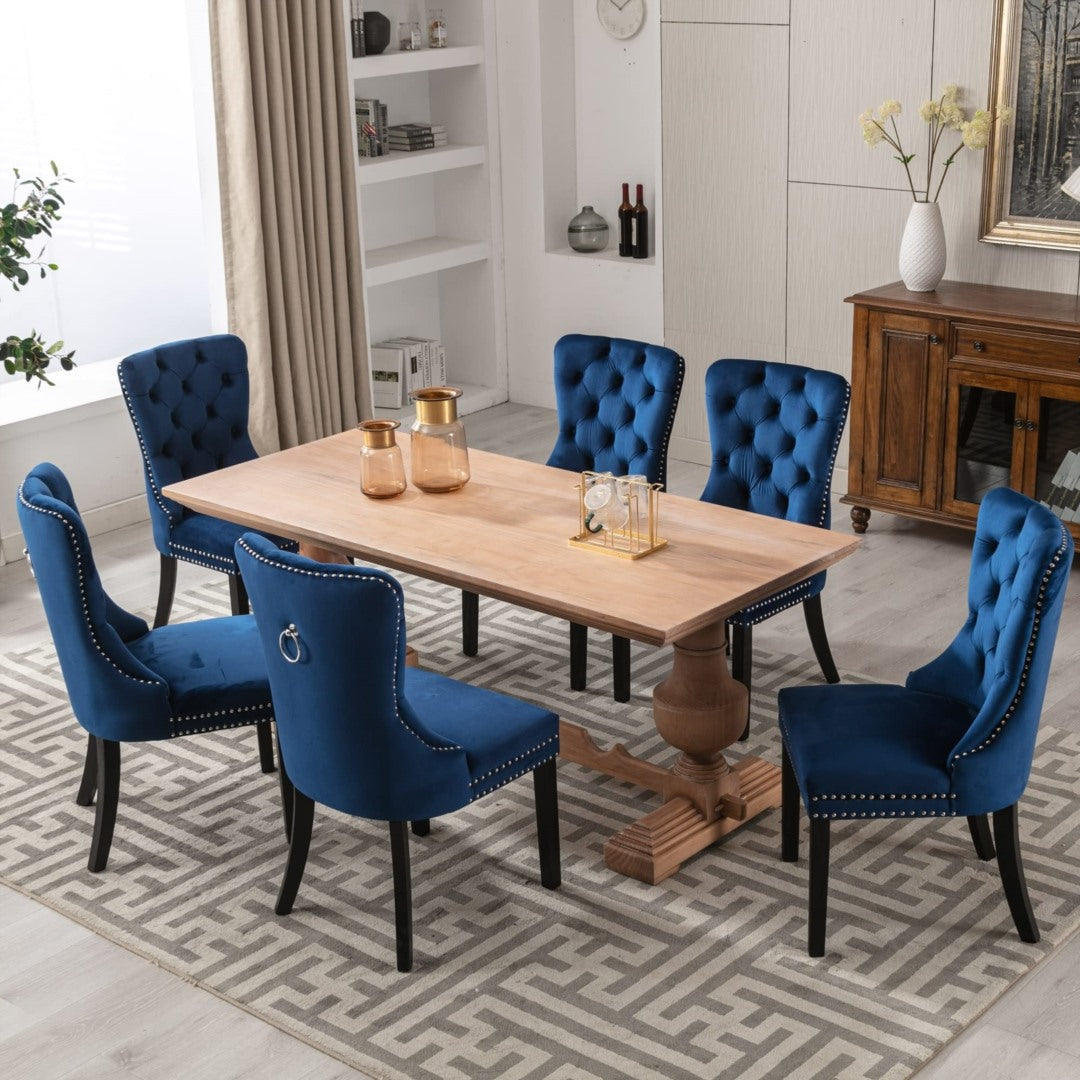 Set of six retro-style blue velvet tufted wingback dining chairs with stud trim and solid dark wood legs around a light wood .