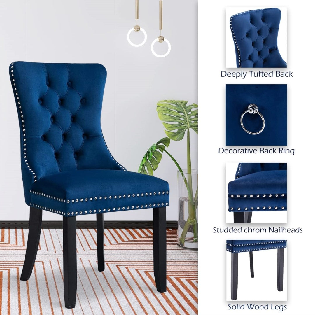 Pair of blue velvet tufted wingback dining chairs with studded nailhead trim and solid wood legs in a bright dining room.