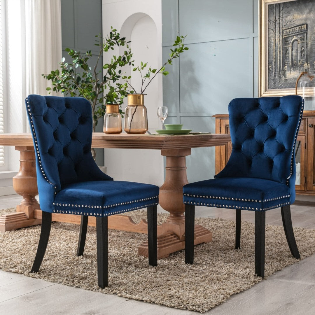 Pair of blue velvet tufted wingback dining chairs with stud trim and solid dark wood legs in elegant vintage dining room.