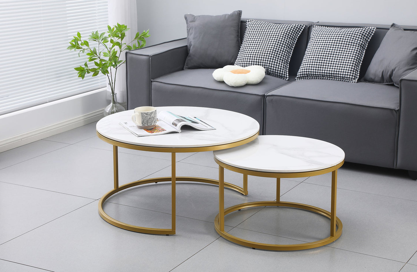 Two nesting round coffee tables with white marble tops and champagne gold metal frames, set on a light gray tiled floor in a .