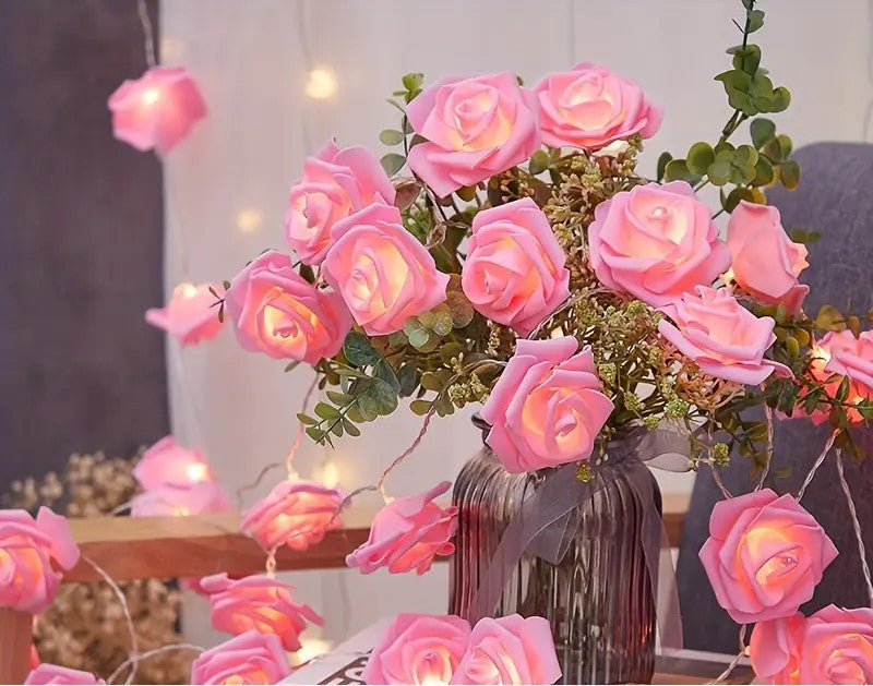 String of 50 pink velvet rose 3D fairy lights draped around a vintage glass vase with pink roses, set in a cozy indoor home.