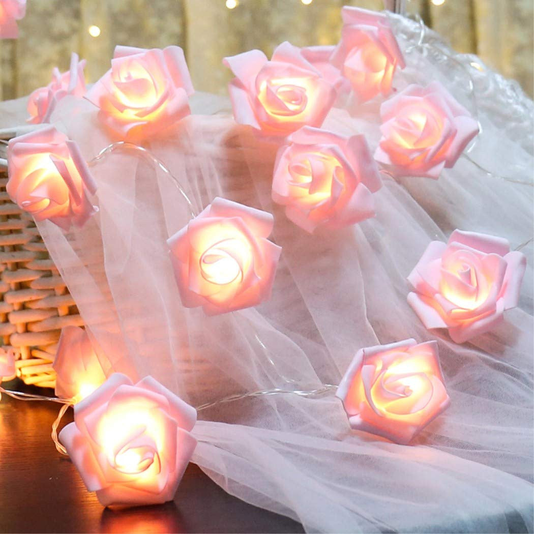 String of 50 pink velvet 3D rose fairy lights glowing softly on sheer white fabric, vintage romantic home decor setting.