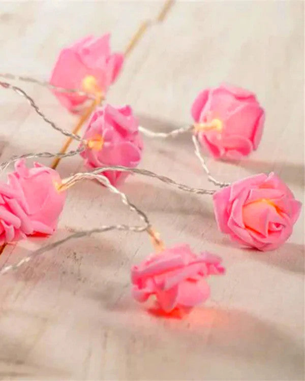 Close-up of pink velvet rose fairy lights with warm glowing bulbs, styled on a light wooden surface for vintage-inspired.