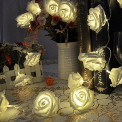 Soft white velvet rose-shaped fairy lights glowing warmly on a vintage lace tablecloth, surrounded by elegant home decor.