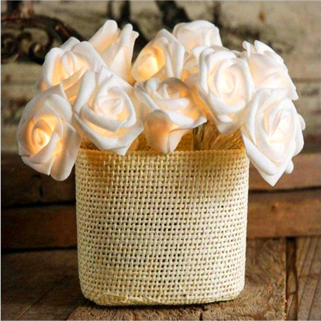 Vintage-inspired white velvet rose fairy lights glowing softly, arranged in a woven basket on rustic wooden surface, evoking .