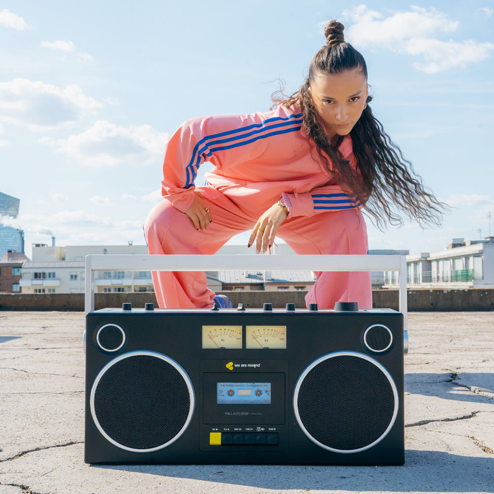 Vintage black Getto Blaster cassette player with silver accents on rooftop under blue sky, styled with casual coral and blue .